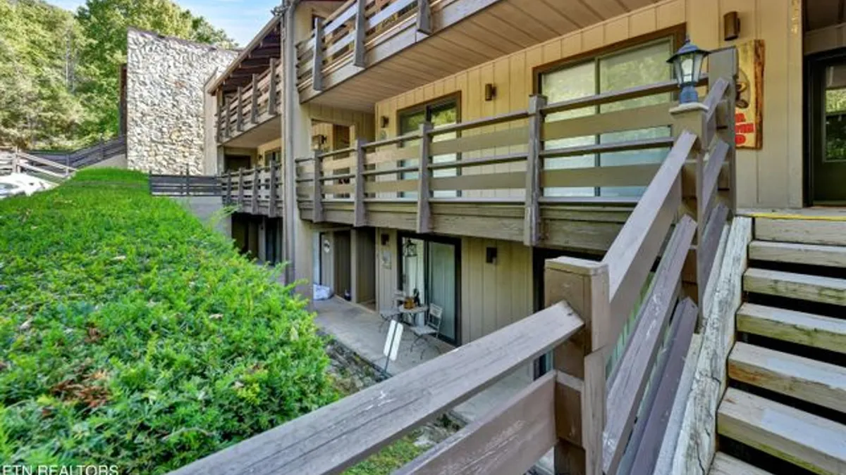 A private balcony with wooden railings and a stone wall, overlooking lush greenery. The scene suggests a serene spot for relaxing outdoors, with the calming influences of nature all around.
