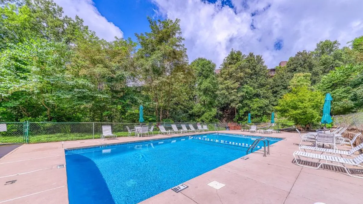 This image presents a bright swimming pool surrounded by inviting lounge chairs and lush greenery. The scene radiates a welcoming atmosphere, perfect for sunbathing, swimming, or gathering with friends. The serene greenery and clear water create a tranquil, resort-like vibe.