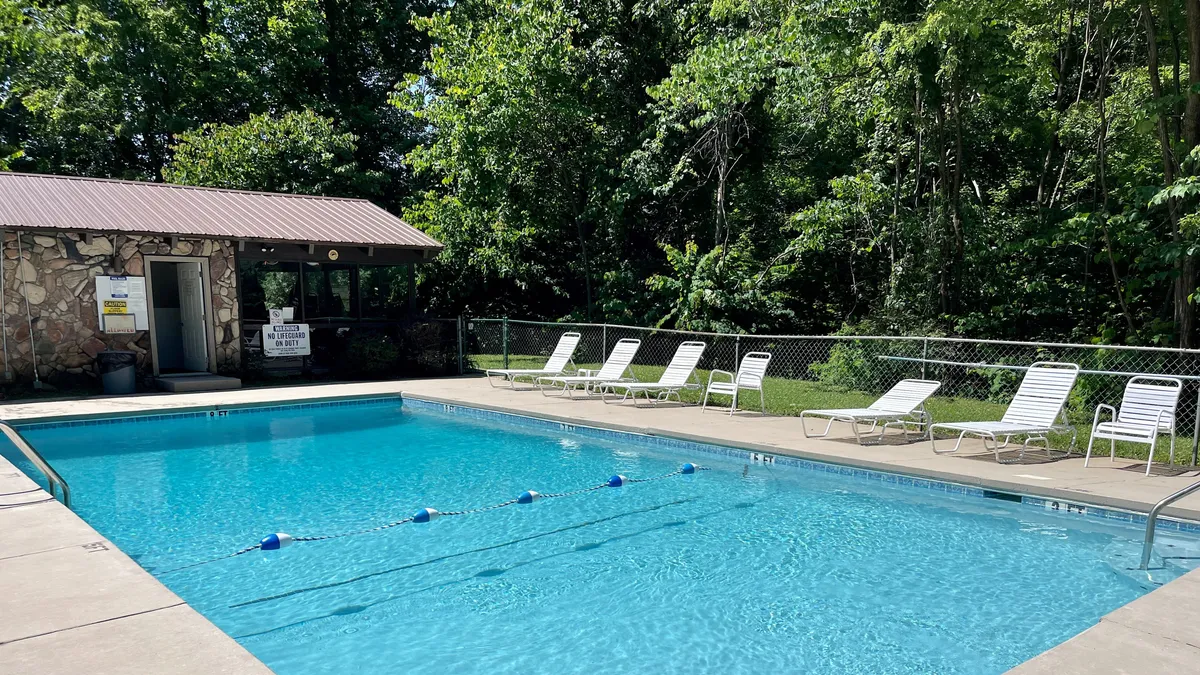 A well-maintained outdoor swimming pool area with lounge chairs arranged invitingly beside the water. A poolside building provides additional amenities, and the scene is bathed in gentle, natural light, enhancing the leisurely, relaxing mood. This is an inviting communal space, ideal for unwinding after a day of adventure.