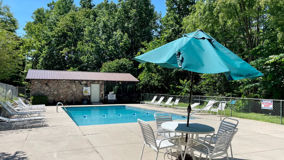 This image captures the community's outdoor swimming pool area, complete with lounge chairs, umbrellas, a poolside table, and a backdrop of tranquil landscaping. The well-maintained pool invites guests to relax, socialize, and enjoy the sunny weather, embodying the spirit of adventure and recreation.