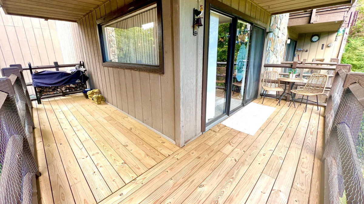 A wooden deck featuring a dining set with chairs and outdoor furniture, visible through glass sliding doors. The image captures the transition between indoor and outdoor spaces, with the deck bathed in morning sunshine and providing a comfortable spot to unwind.