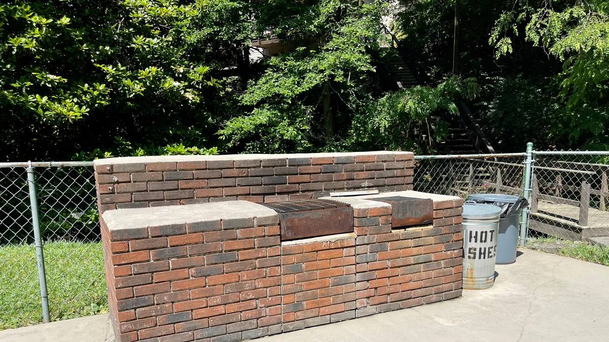 The photo features a communal brick seating area with a built-in grill surface and trash can, ideal for outdoor cooking and social gatherings. The friendly, open layout provides a glimpse of how residents and guests can come together for barbecues and meals al fresco.
